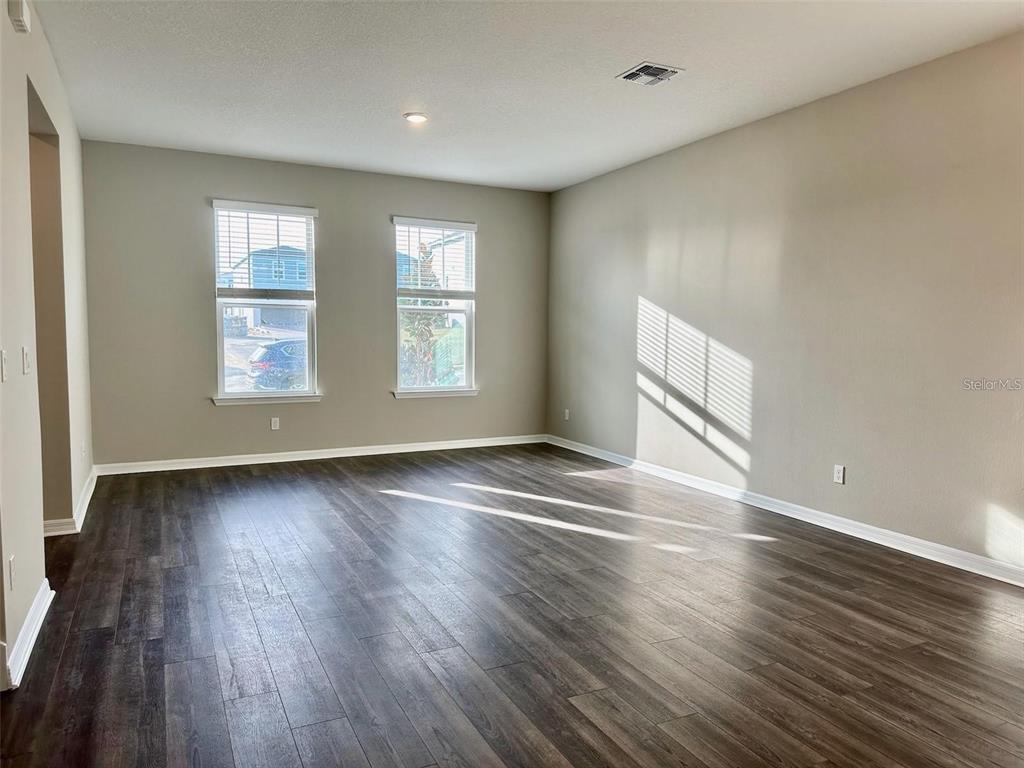 An empty room features dark wood-look flooring, light gray walls, and two windows — 4869 LACEWING DRIVE, WINTER GARDEN, FL