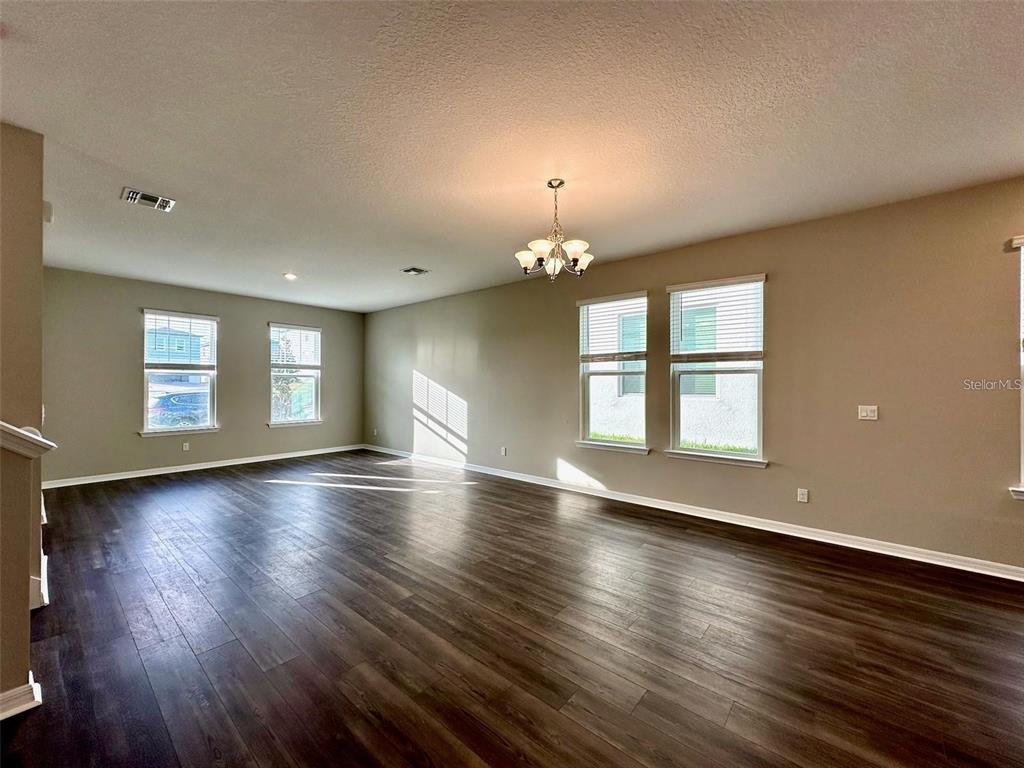A spacious living room features dark wood-look flooring, neutral walls, and a central chandelier — 4869 LACEWING DRIVE, WINTER GARDEN, FL