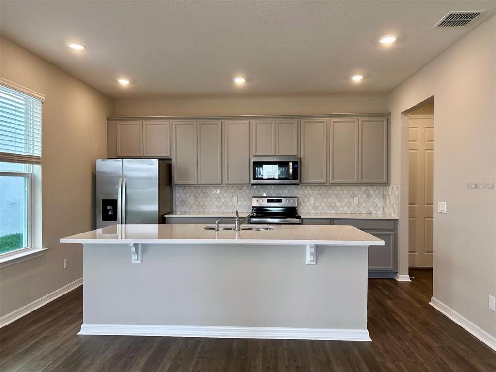 A modern kitchen features gray cabinets, stainless steel appliances, and a large white island — 4869 LACEWING DRIVE, WINTER GARDEN, FL