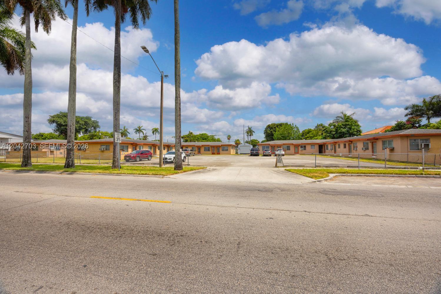 A single-story apartment complex with a paved parking lot sits behind a chain-link fence — 1915 NW 28th St, Miami FL 33142, MIAMI, FL
