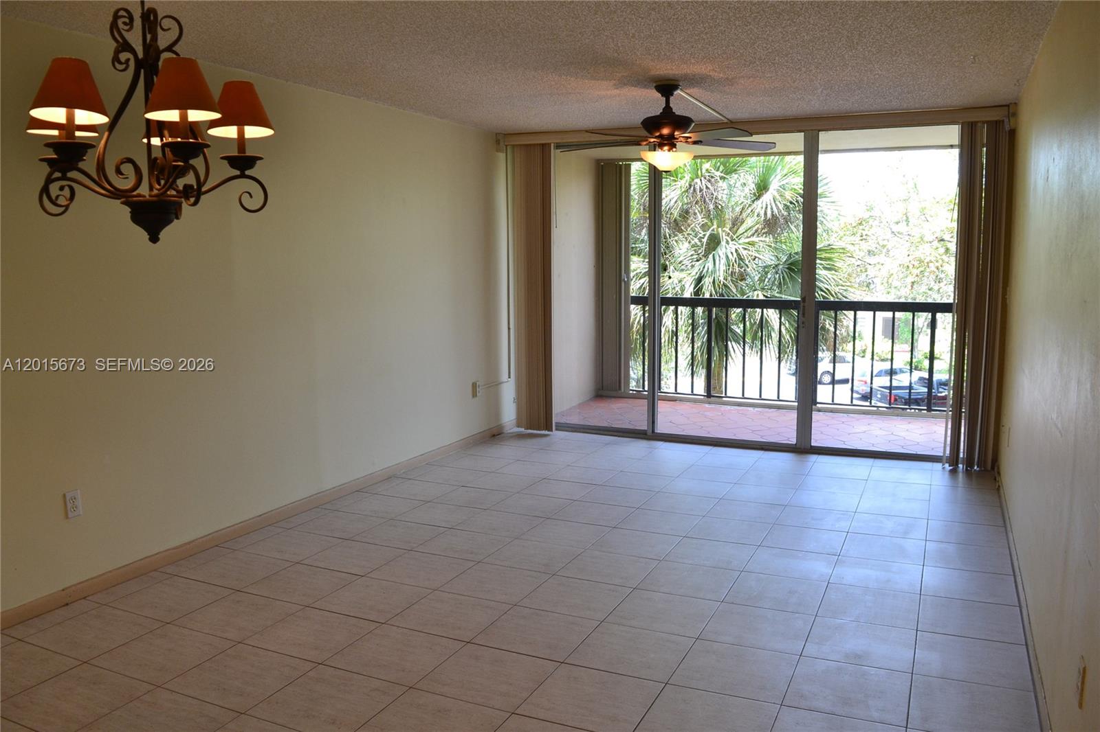An empty room features tile flooring, a chandelier, a ceiling fan, and sliding glass balcony doors — 10855 SW 112th Ave # 309, Miami FL 33176, MIAMI, FL