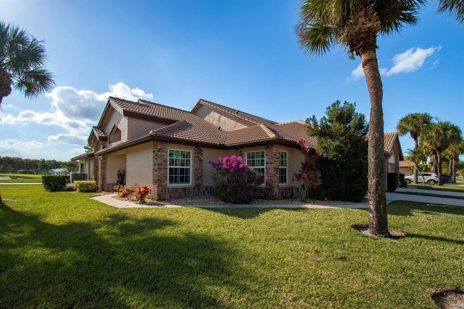 A tan stucco house with a tiled roof and brick accents sits on a grassy lawn — 8213 Cassia Drive, Boynton Beach FL 33472, BOYNTON BEACH, FL