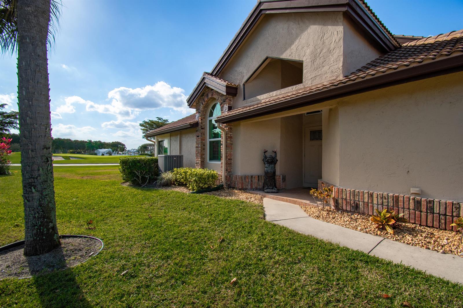 A tan house with a brick-accented entryway and a palm tree on a golf course — 8213 Cassia Drive, Boynton Beach FL 33472, BOYNTON BEACH, FL