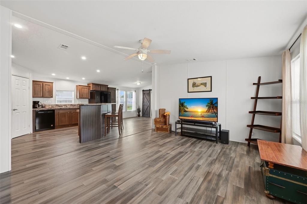 An open-concept living room and kitchen featuring wood-look flooring, white walls, and dark cabinetry — 209 ELLSWORTH DRIVE, KISSIMMEE, FL