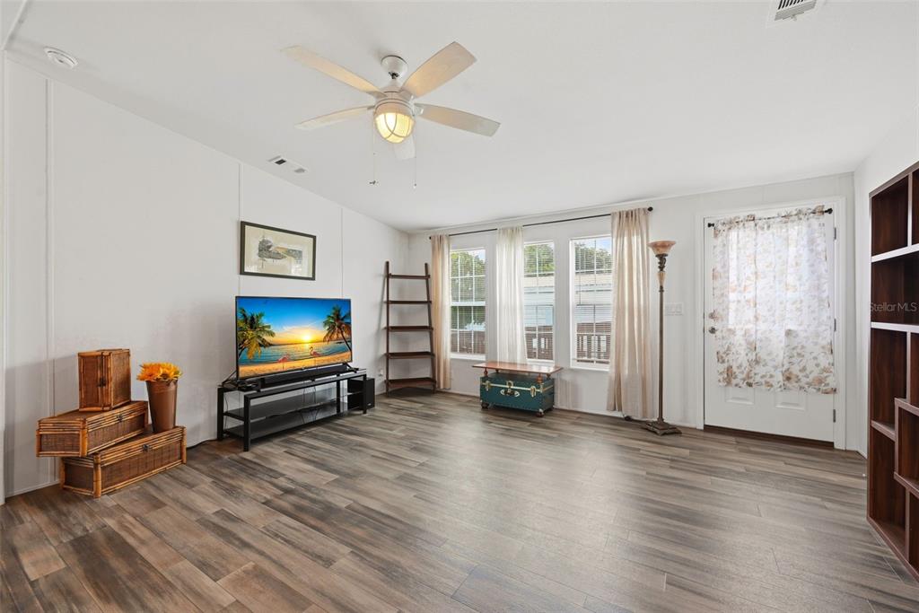 A living room features wood-look flooring, a ceiling fan, a television, and a front door — 209 ELLSWORTH DRIVE, KISSIMMEE, FL