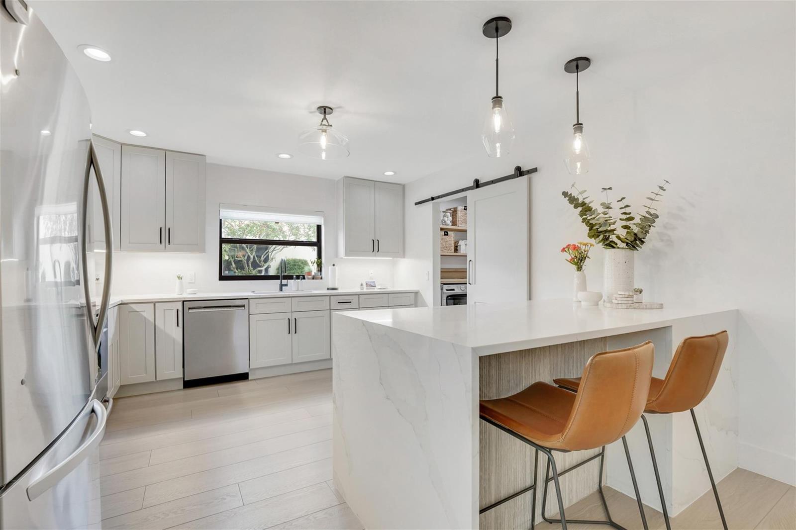 A modern kitchen features white cabinets, a marble-topped island with leather stools, and stainless appliances — 8569 Casa Del Lago, Boca Raton FL 33433, BOCA RATON, FL