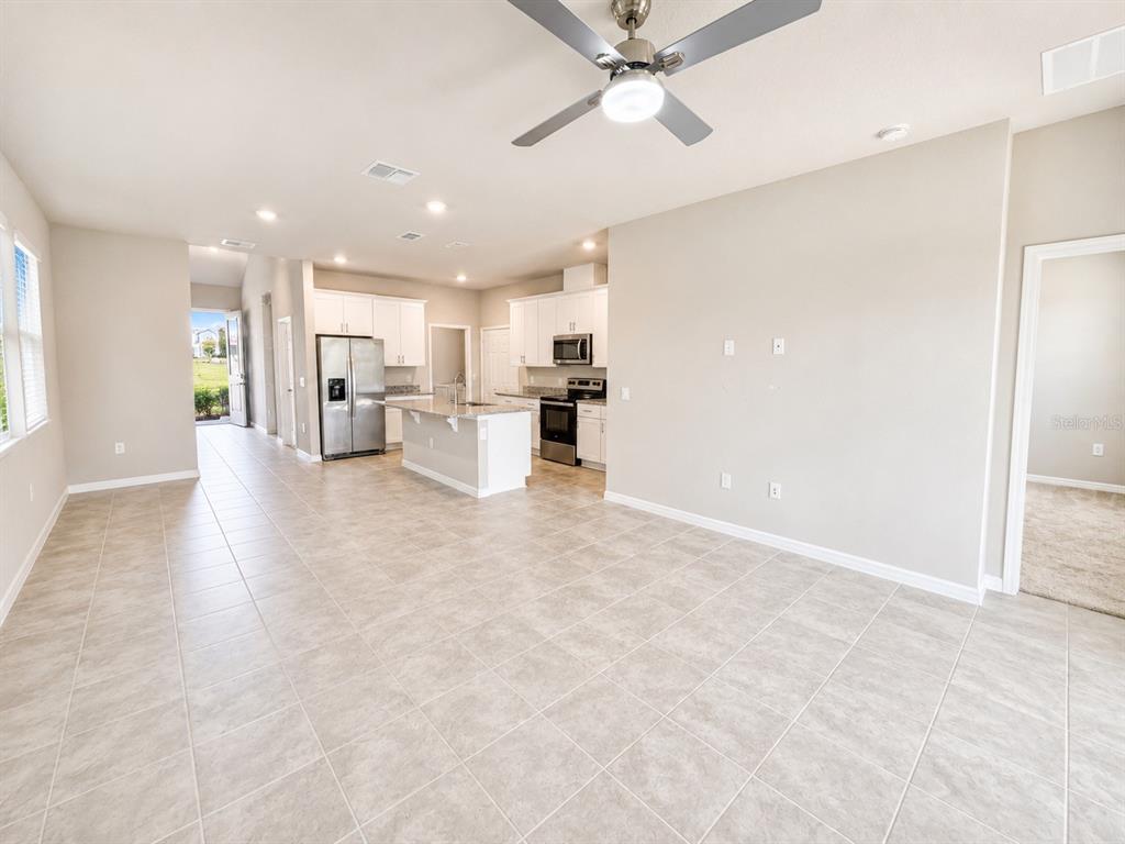 An open-concept kitchen and living area features light tile flooring, white cabinetry, and stainless appliances — 2269 MYSTIC MAZE LANE, MINNEOLA, FL