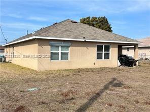 The rear exterior of a tan stucco house features a covered patio and shingled roof — 3815 SW 11th Pl, Cape Coral FL 33914, CAPE CORAL, FL