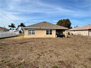 The exterior rear view of a single-story house with a tan stucco facade and yard — 3815 SW 11th Pl, Cape Coral FL 33914, CAPE CORAL, FL