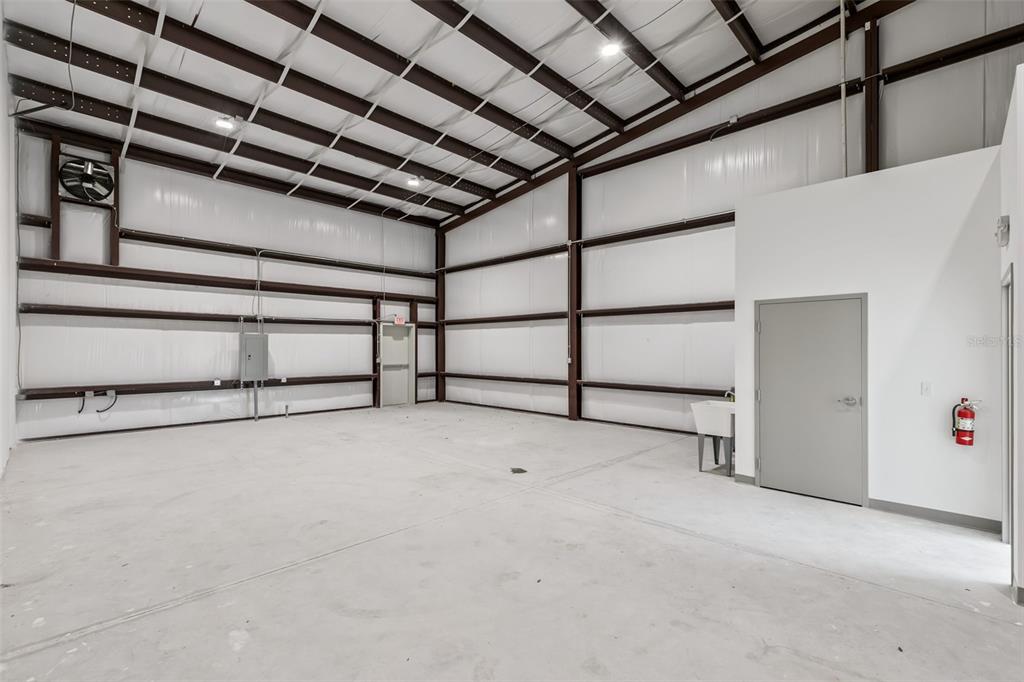 An empty industrial warehouse space features white metal walls, a concrete floor, and two doors — 7120 SAMPEY ROAD UNIT 103, GROVELAND, FL