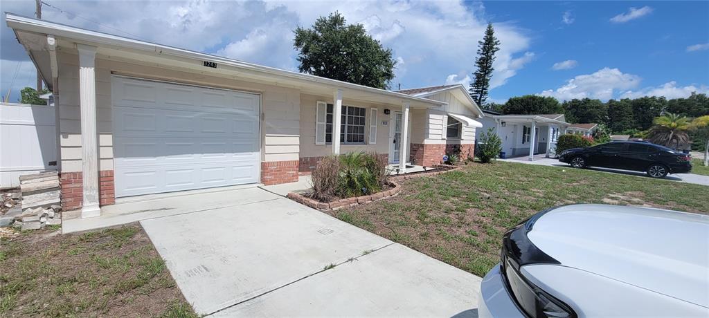 A single-story house with a white garage door, brick accents, and a concrete driveway — 3243 BAYPORT DRIVE, HOLIDAY, FL
