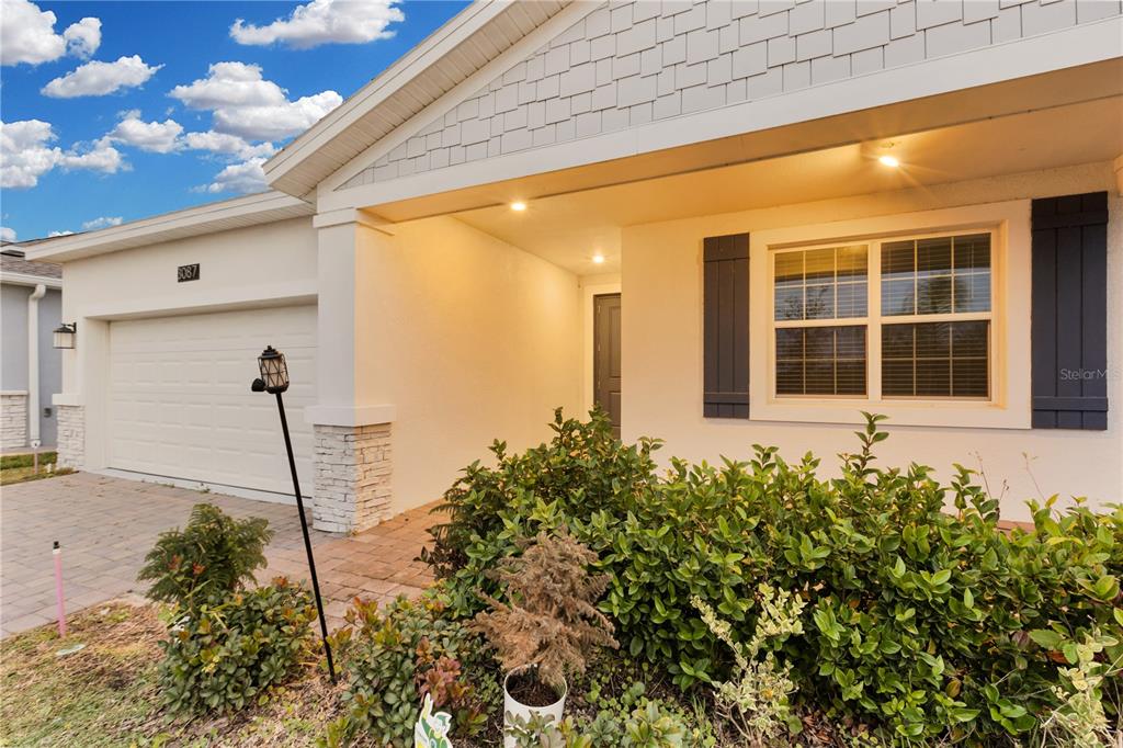 The exterior of a single-story house features a white garage, a covered entryway, and landscaping — 3087 CAMDEN WAY, DAVENPORT, FL