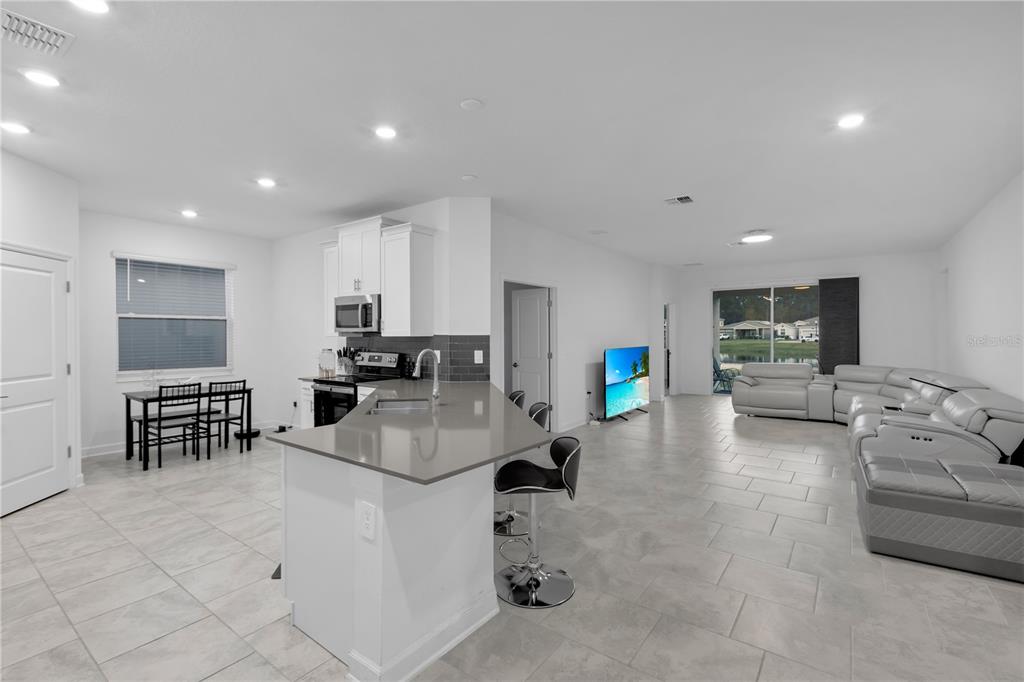 An open-concept kitchen and living area with white cabinets, gray countertops, and light tile flooring — 3087 CAMDEN WAY, DAVENPORT, FL