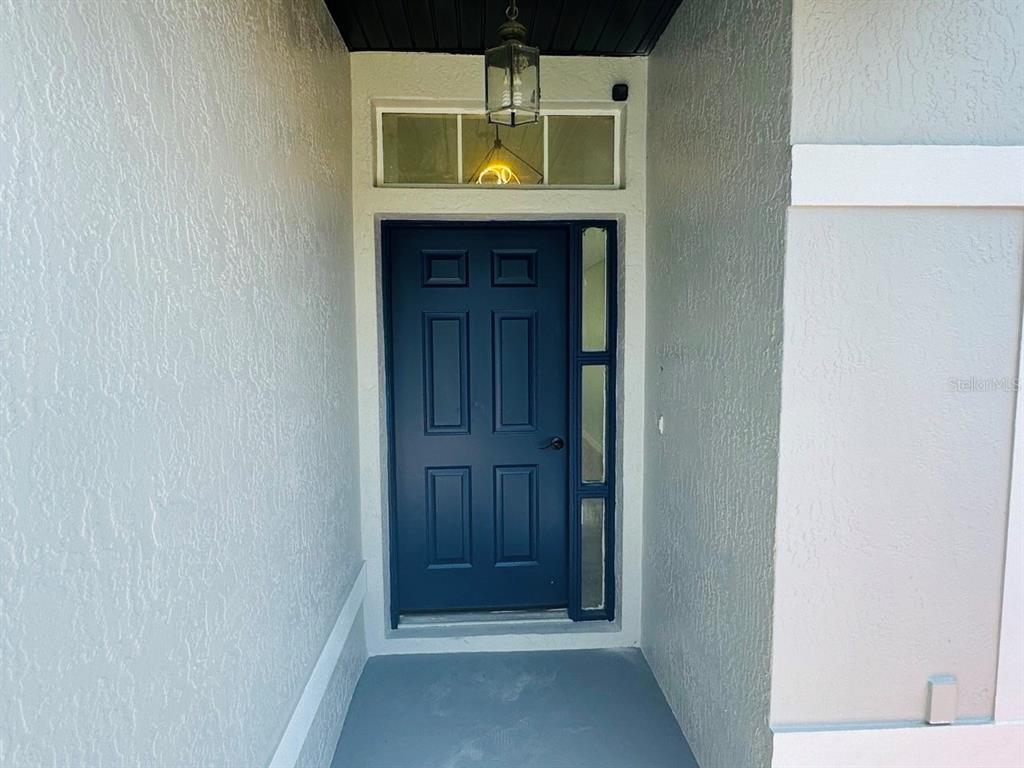 A blue front door with a side window and transom sits in a covered entryway — 215 HOLLOWBROOK CIRCLE, DAYTONA BEACH, FL
