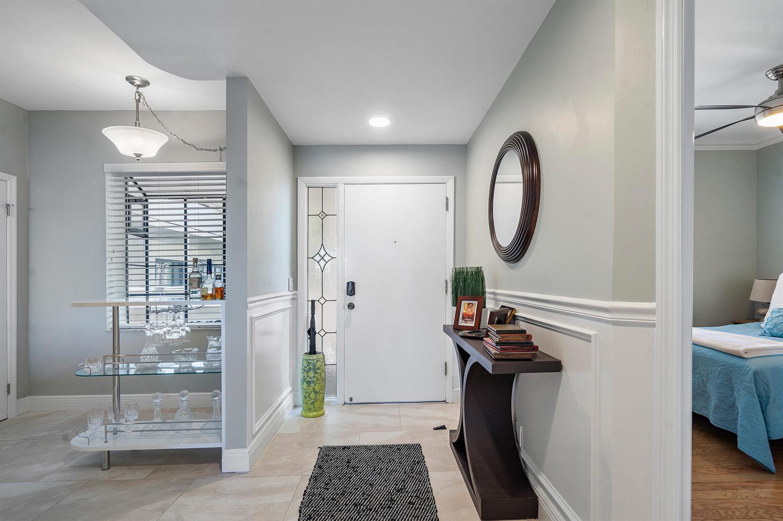 An entryway features a white door, a glass console table, a bar area, and wainscoting — 200 Waterway Road # 204, Tequesta FL 33469, TEQUESTA, FL
