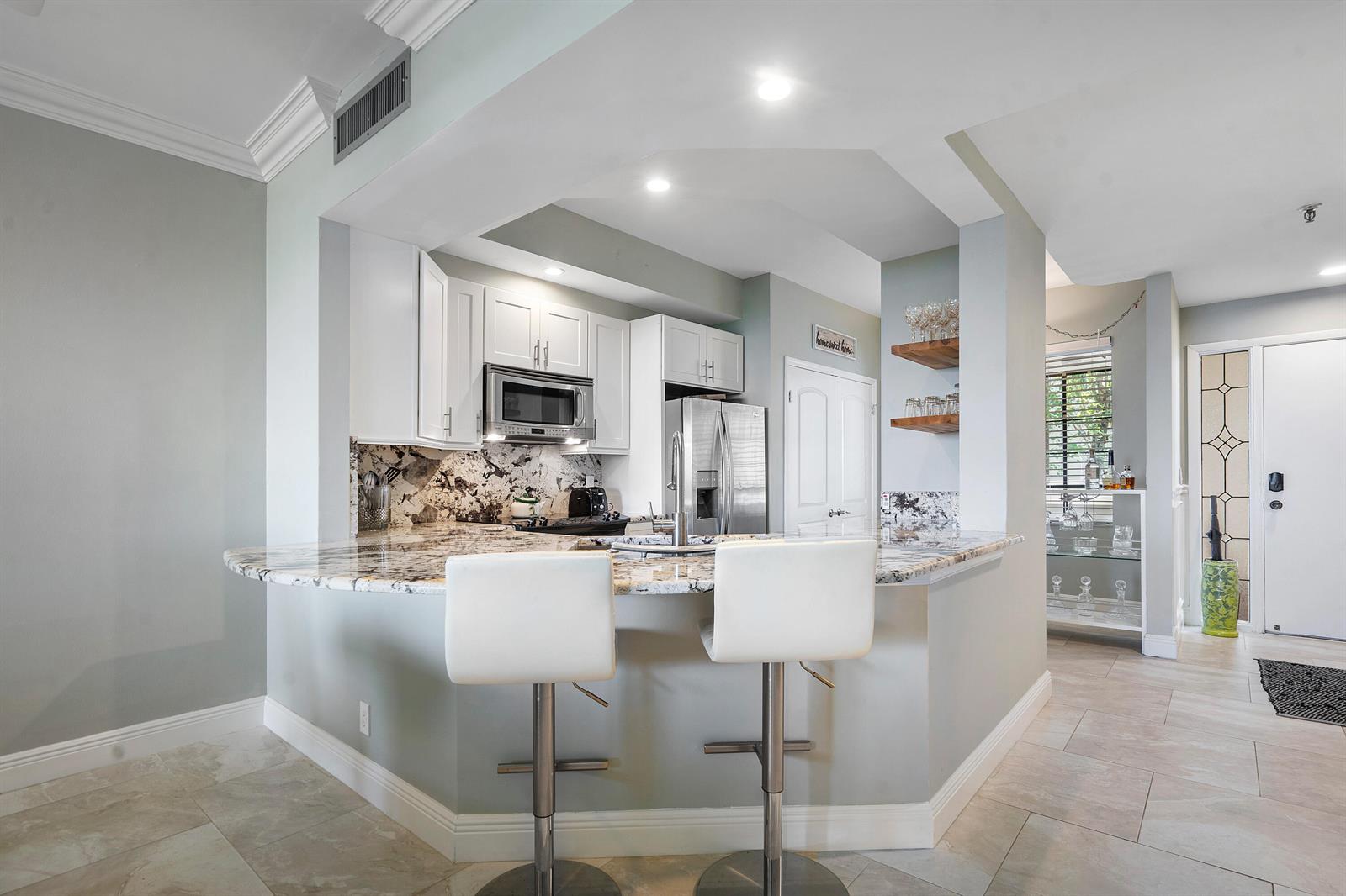 A kitchen features white cabinets, granite countertops, a breakfast bar with two stools, and tile flooring — 200 Waterway Road # 204, Tequesta FL 33469, TEQUESTA, FL