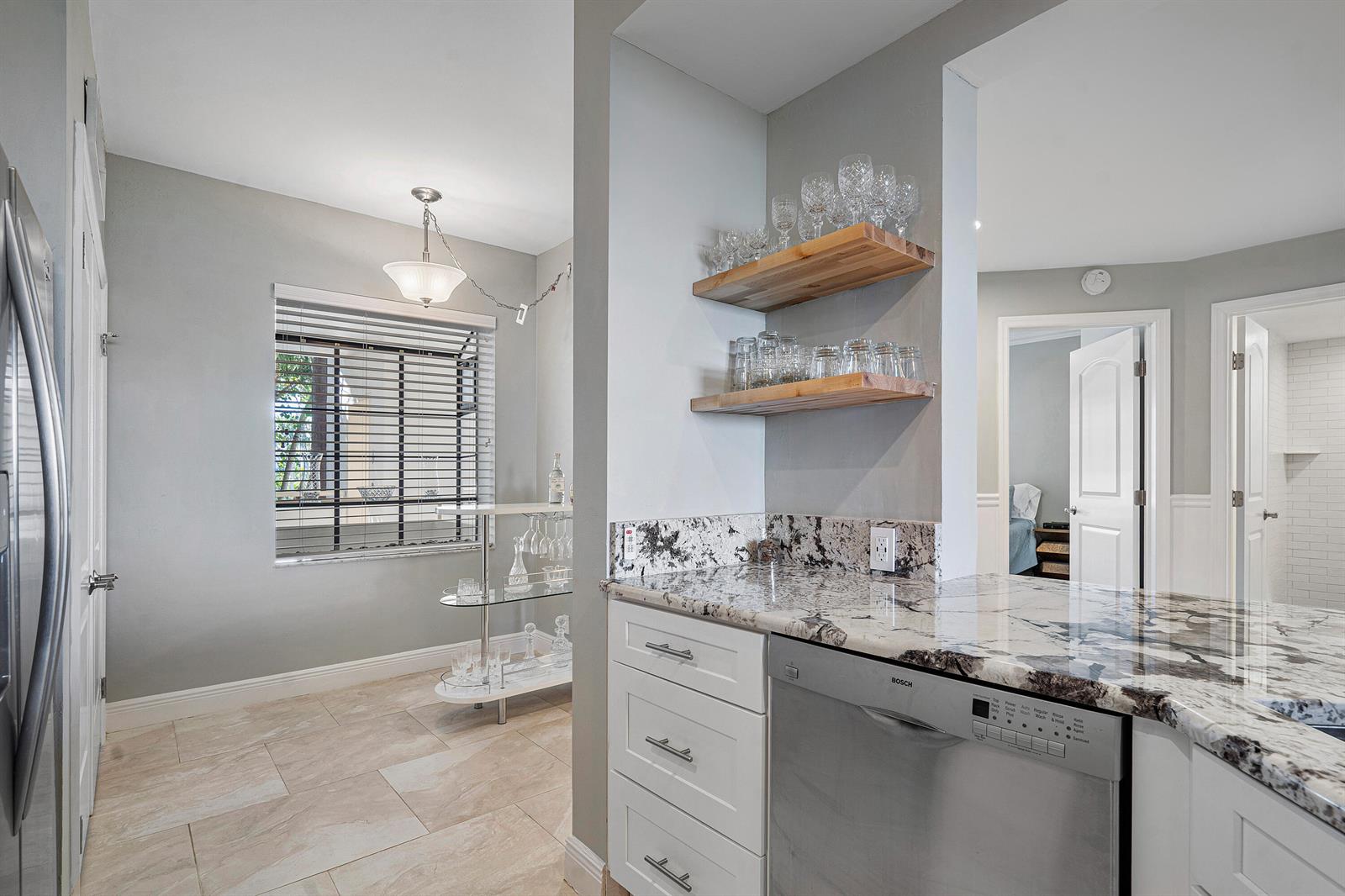 A kitchen area features white cabinets, granite countertops, a stainless dishwasher, and open wooden shelving — 200 Waterway Road # 204, Tequesta FL 33469, TEQUESTA, FL