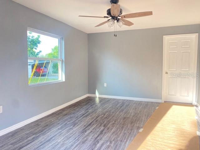 An empty room features gray walls, wood-look flooring, a ceiling fan, and a white door — 6246-6248 20TH STREET, ZEPHYRHILLS, FL