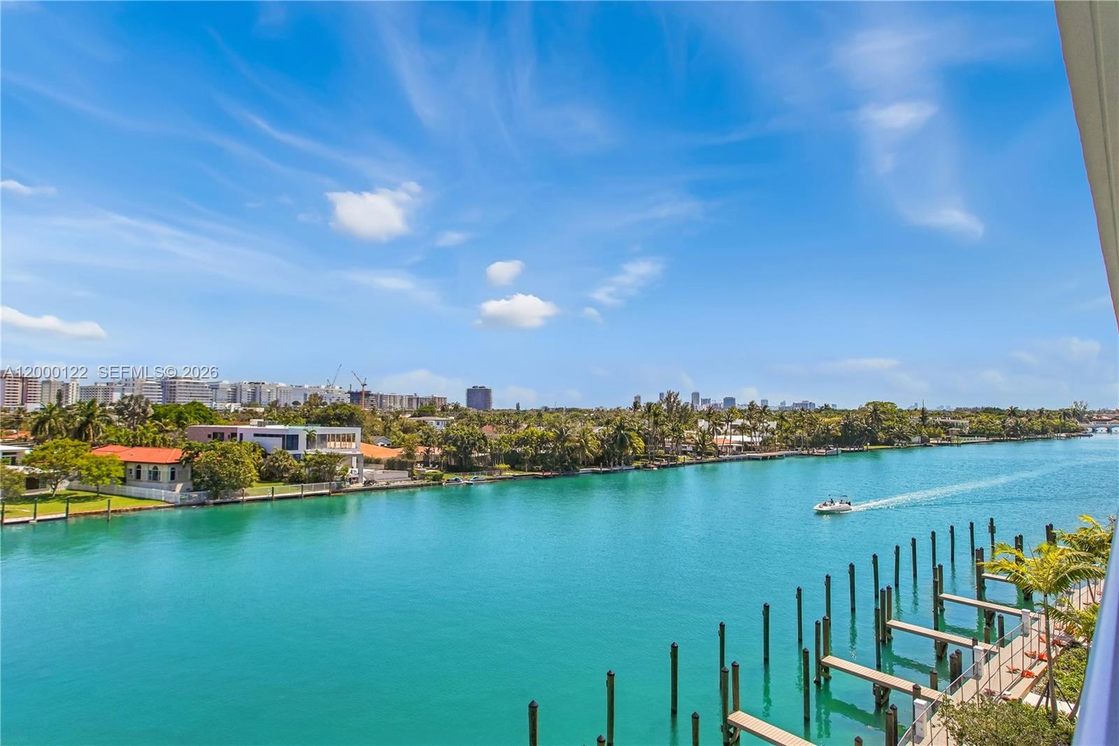 An elevated view of a turquoise canal with boat docks and a distant city skyline — BAY HARBOR ISLANDS, FL