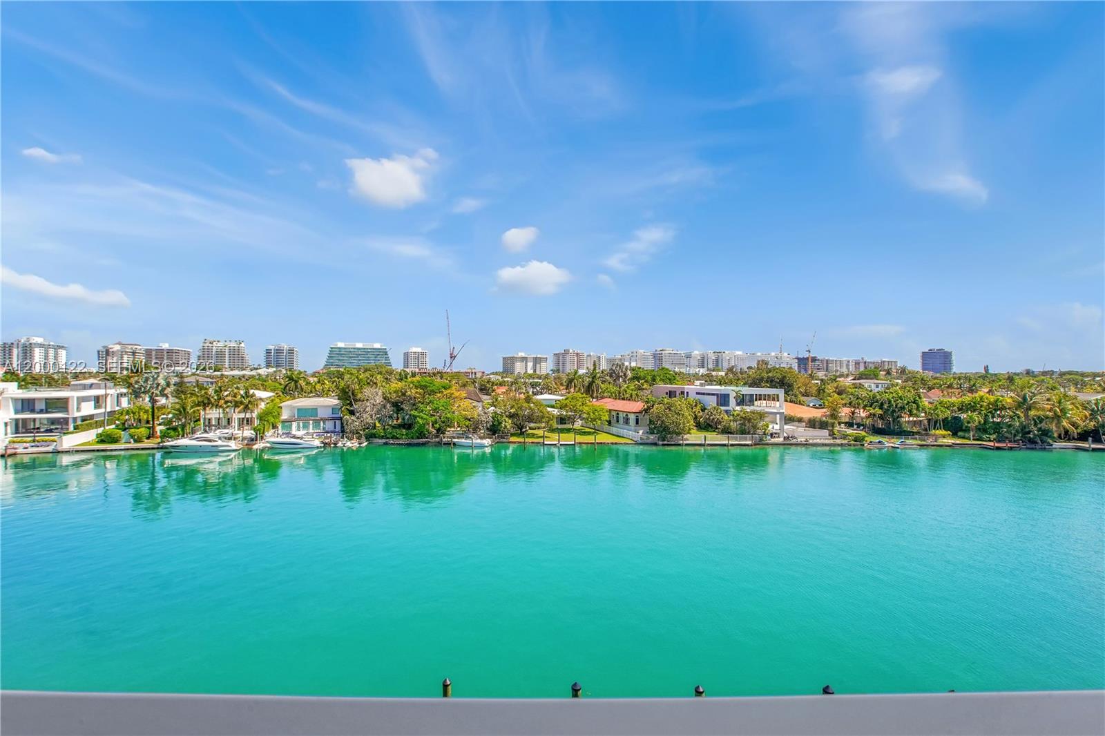 A wide view of a turquoise waterway with waterfront homes and a distant city skyline — BAY HARBOR ISLANDS, FL