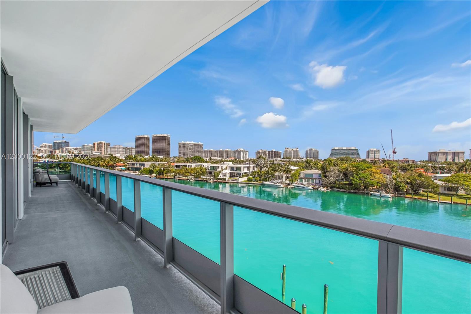 A high-rise balcony overlooks a turquoise canal with luxury homes and city buildings beyond — BAY HARBOR ISLANDS, FL