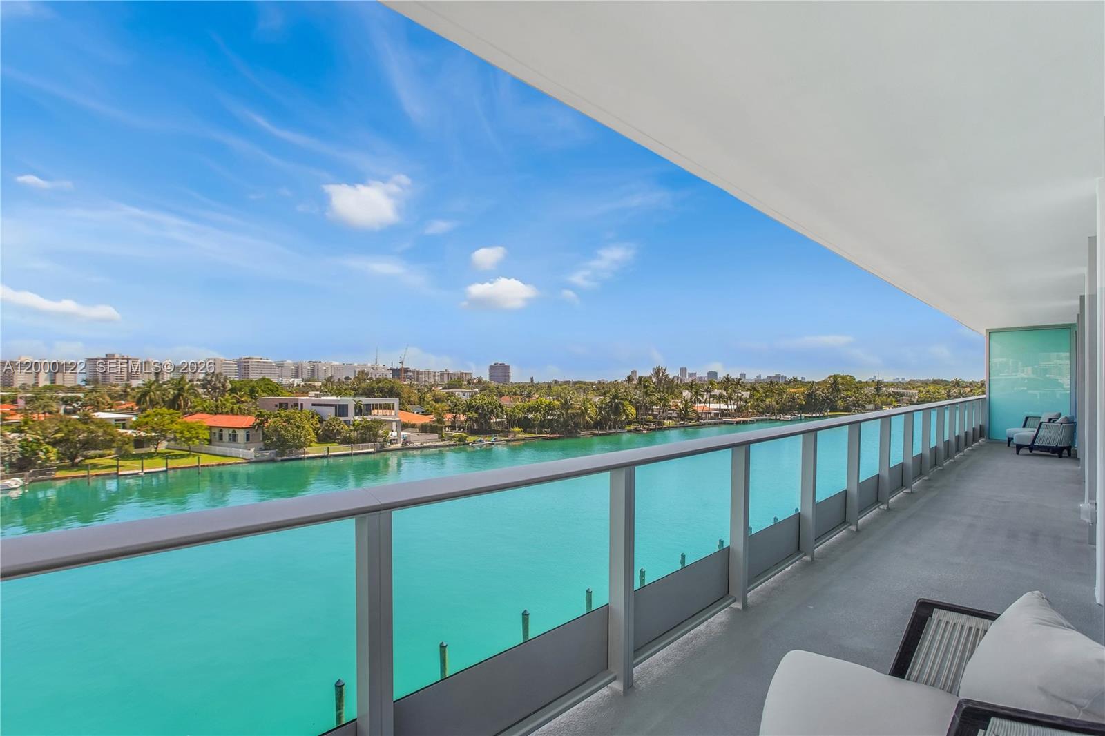 A balcony with a glass railing overlooks a turquoise waterway and a city skyline — BAY HARBOR ISLANDS, FL