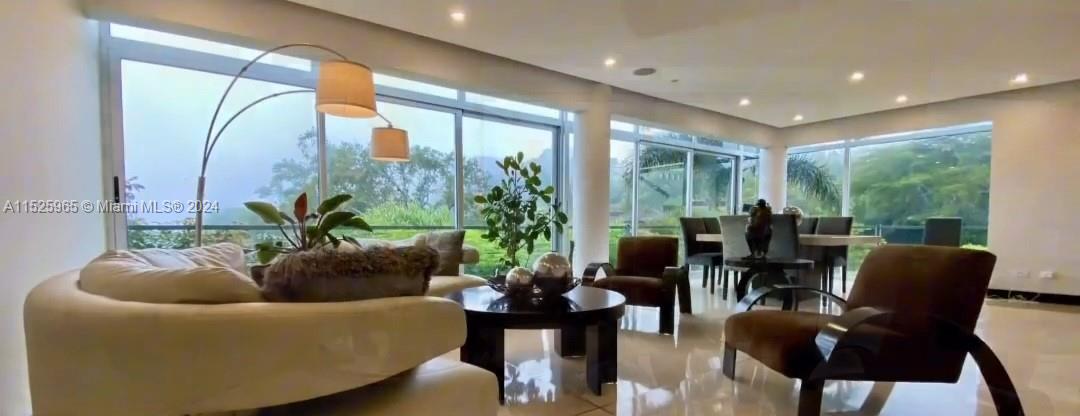 A modern living room features floor-to-ceiling windows, white tile floors, and a curved sofa — Eco Residencial Vila Real Pozos de Santa Ana, SJ, SJ