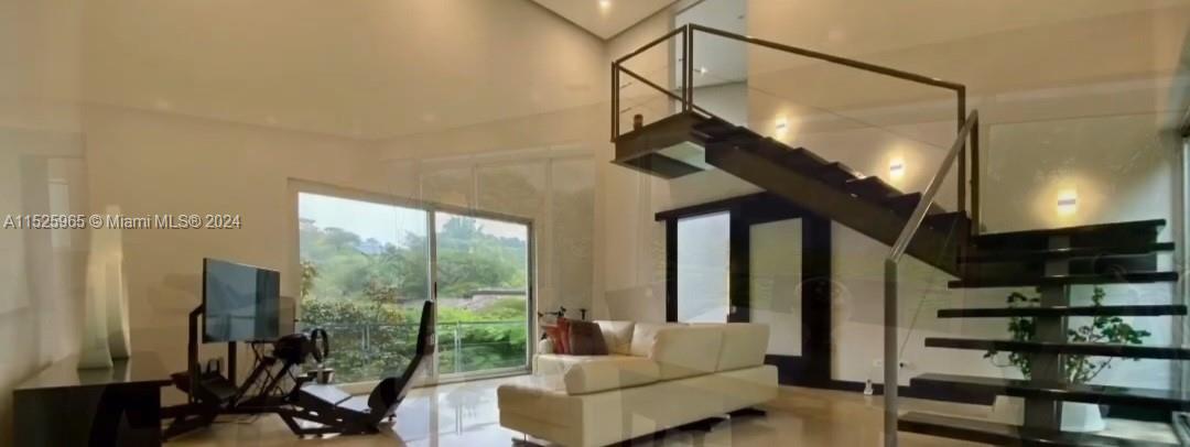 A modern living room features a white sofa, a racing simulator, and a floating staircase — Eco Residencial Vila Real Pozos de Santa Ana, SJ, SJ