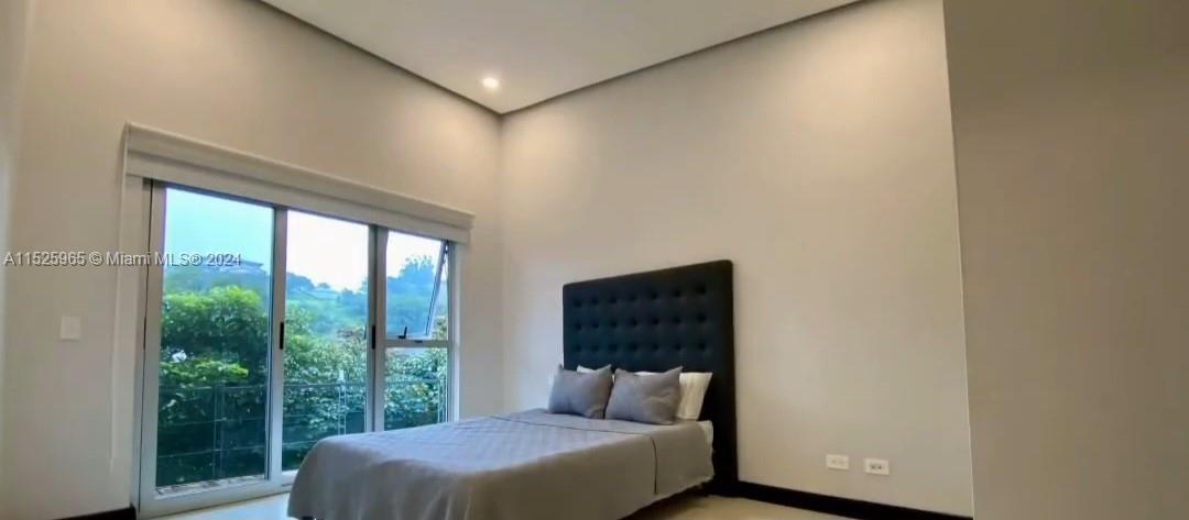 A bedroom features a tufted black headboard, light-colored walls, and a large sliding glass door — Eco Residencial Vila Real Pozos de Santa Ana, SJ, SJ