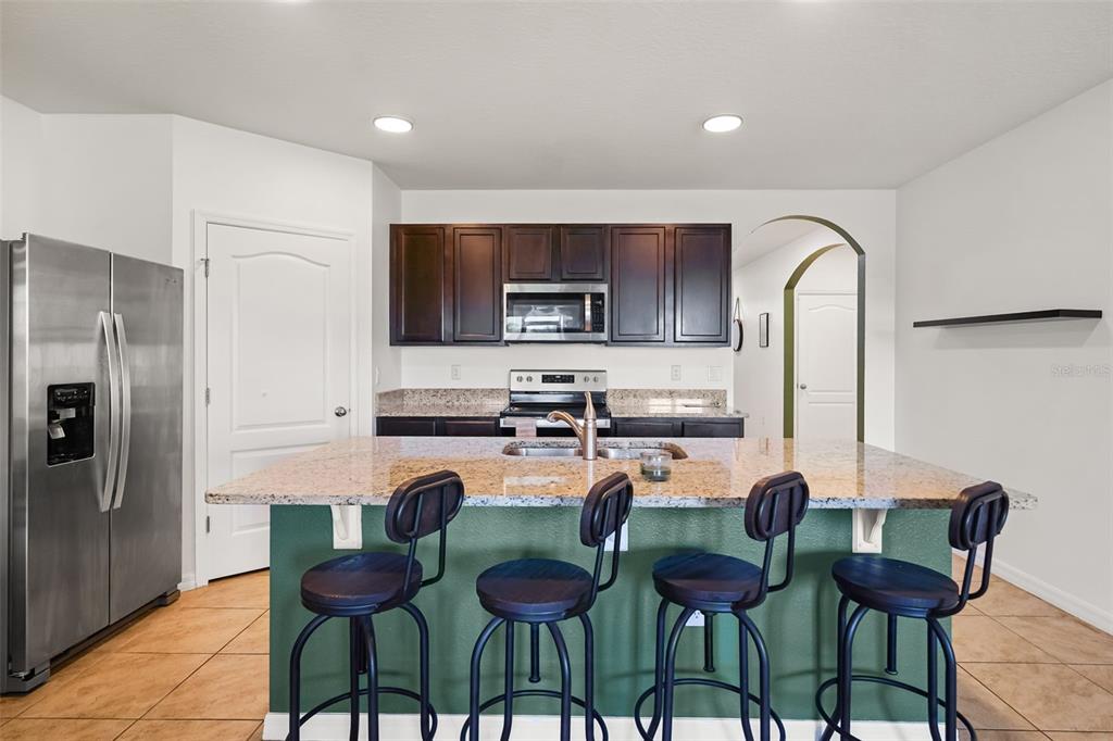 A kitchen features a granite-topped island with four bar stools and dark wood cabinetry — 860 BROOKLET DRIVE, DAVENPORT, FL