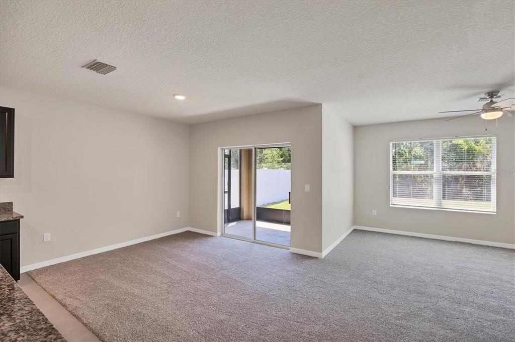 An empty living room with gray carpeting, a ceiling fan, and sliding glass patio doors — 153 TIERRA VERDE WAY, BRADENTON, FL