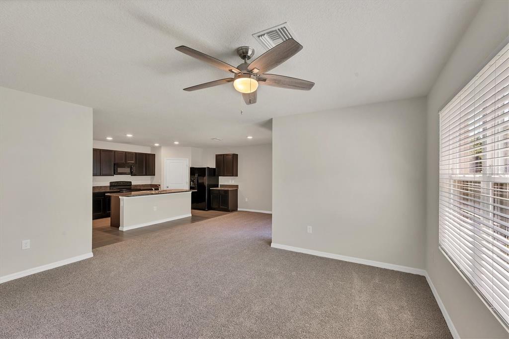 A living room with carpeted flooring opens into a kitchen with dark cabinetry and appliances — 153 TIERRA VERDE WAY, BRADENTON, FL