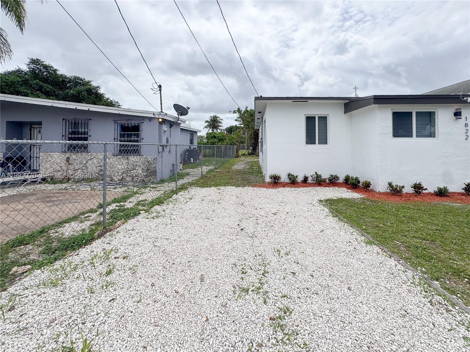 A white house and a gray house are separated by a gravel driveway and fence — 1822 NW 66th St, Miami FL 33147, MIAMI, FL