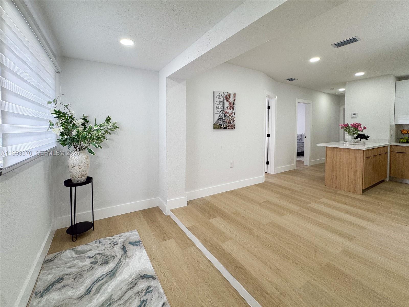 A bright, open-concept living area features light wood flooring, white walls, and a kitchen island — 1822 NW 66th St, Miami FL 33147, MIAMI, FL
