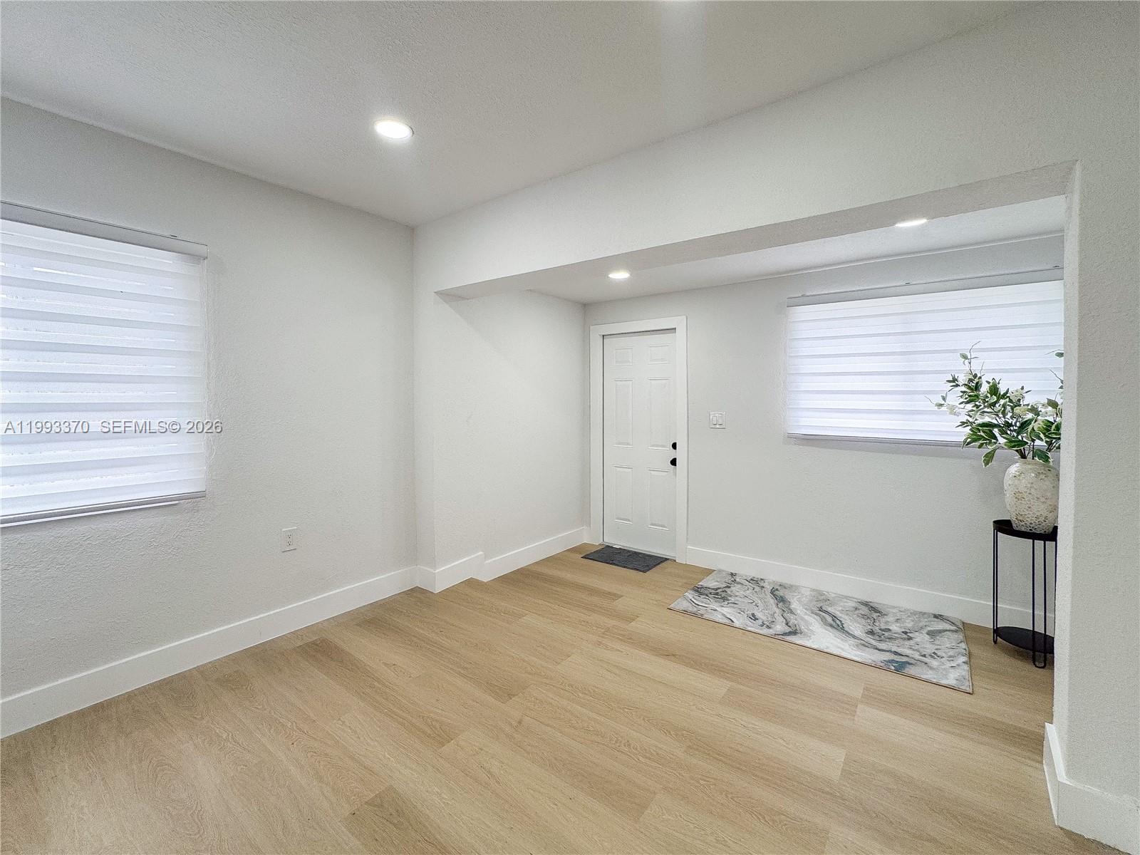 A bright room features light wood-look flooring, white walls, recessed lighting, and a white door — 1822 NW 66th St, Miami FL 33147, MIAMI, FL