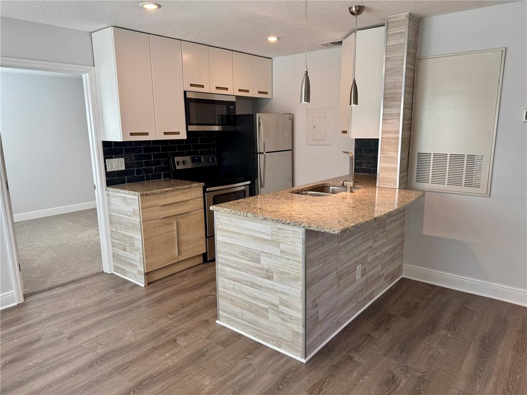 A kitchen features white upper cabinets, wood-look lower cabinets, granite countertops, and a black backsplash — 2585 GRASSY POINT DRIVE UNIT 111, LAKE MARY, FL