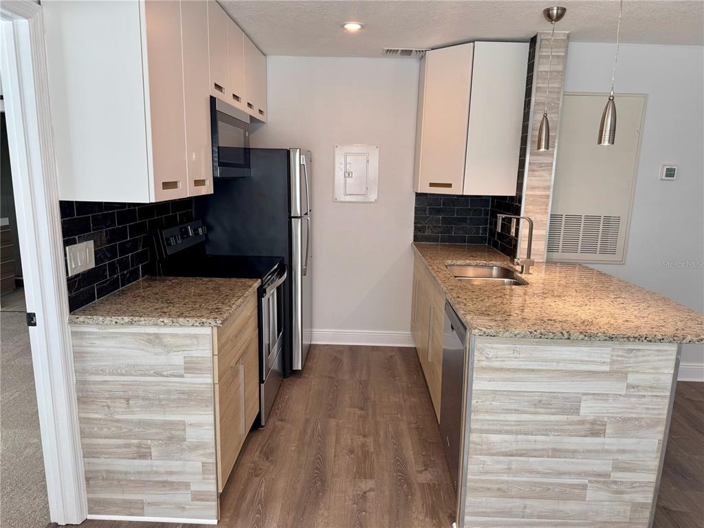 A galley kitchen features light wood-look cabinets, granite countertops, and a black subway tile backsplash — 2585 GRASSY POINT DRIVE UNIT 111, LAKE MARY, FL