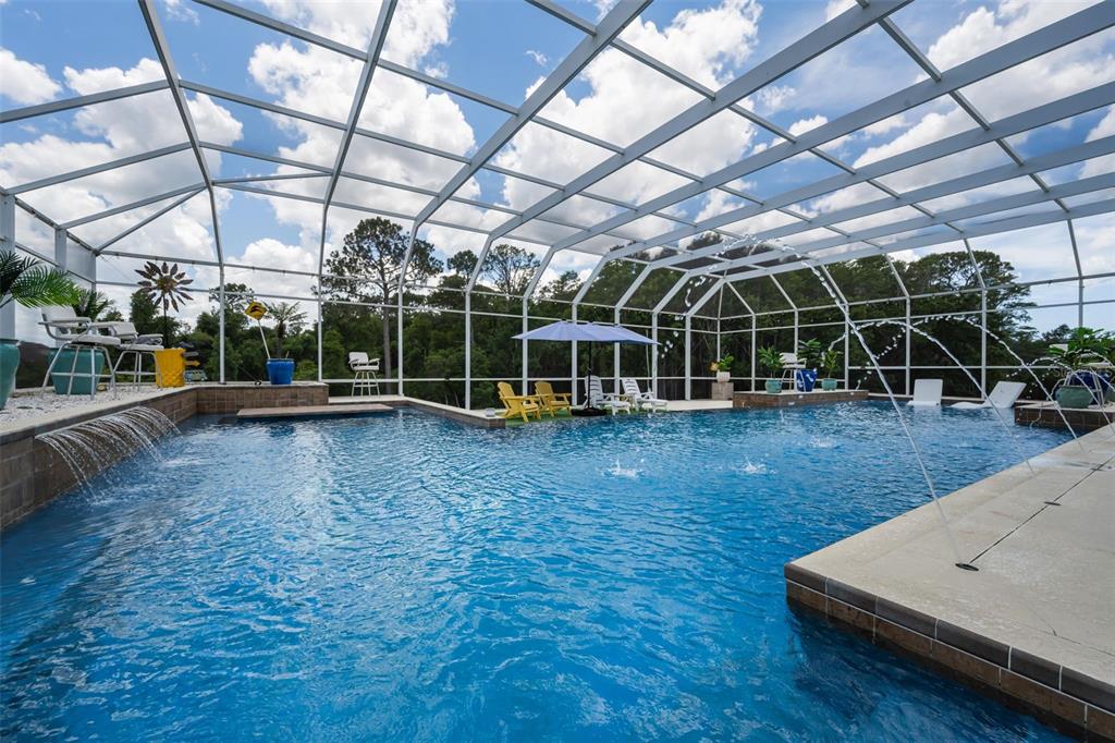 A screened-in swimming pool features a waterfall, water jets, and patio furniture on the deck — 11046 LAKEVIEW DRIVE, NEW PORT RICHEY, FL