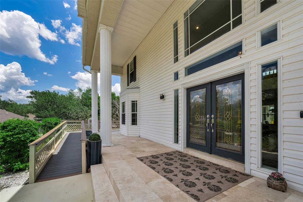 A white-sided house exterior features a stone porch, double glass doors, and a wooden ramp — 11046 LAKEVIEW DRIVE, NEW PORT RICHEY, FL