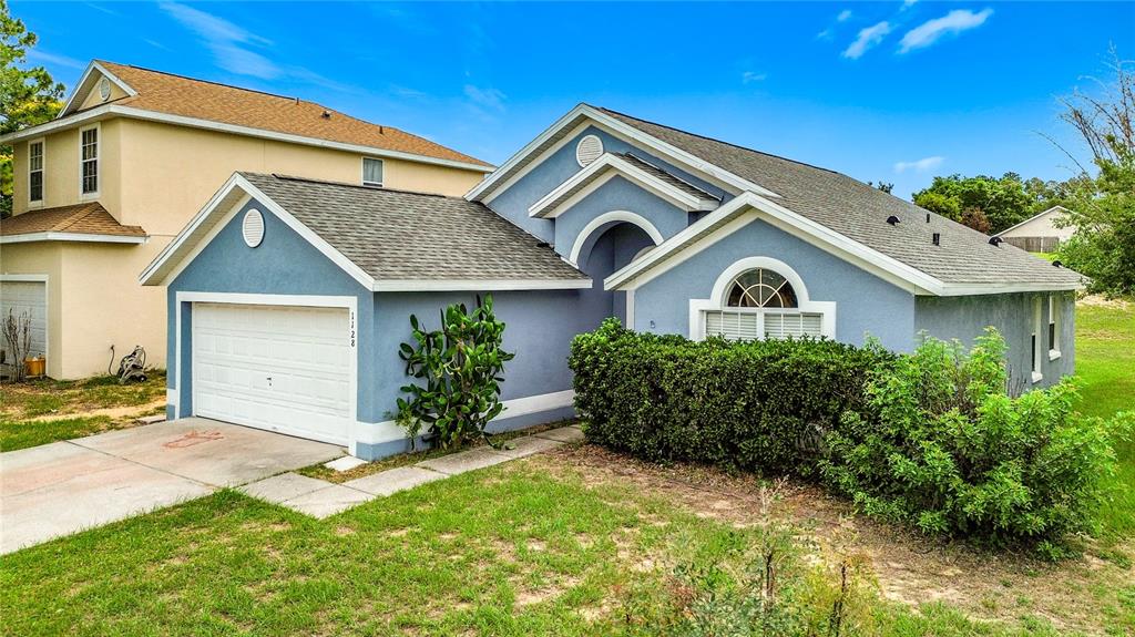 A blue single-story house with a white garage door and a large front hedge — 1128 PINEDALE DRIVE, DAVENPORT, FL