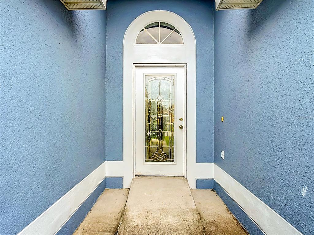A white front door with a decorative glass insert sits within a blue stucco entryway — 1128 PINEDALE DRIVE, DAVENPORT, FL
