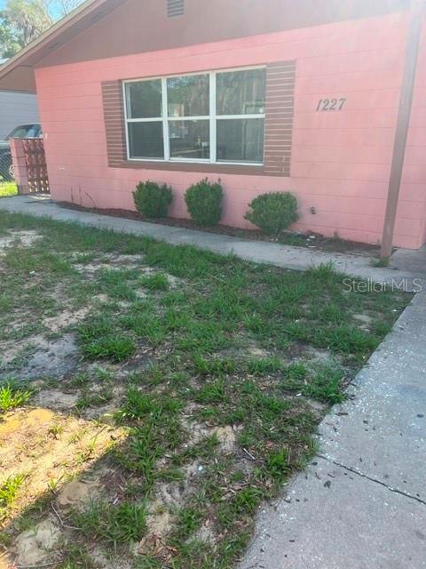 The exterior of a pink, single-story house features a large window and a concrete walkway — 1227 SE 19TH TERRACE, GAINESVILLE, FL