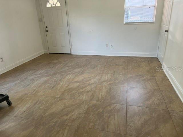 An empty room features tan tile flooring, white walls, a white door, and a window — 1227 SE 19TH TERRACE, GAINESVILLE, FL