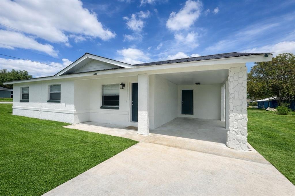 A white single-story house with a carport and a stone pillar under a blue sky — 1004 BOOKER AVENUE, SEBRING, FL