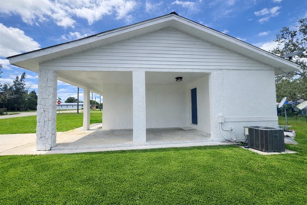 A white house exterior features a covered carport with stone-accented pillars and a grassy lawn — 1004 BOOKER AVENUE, SEBRING, FL