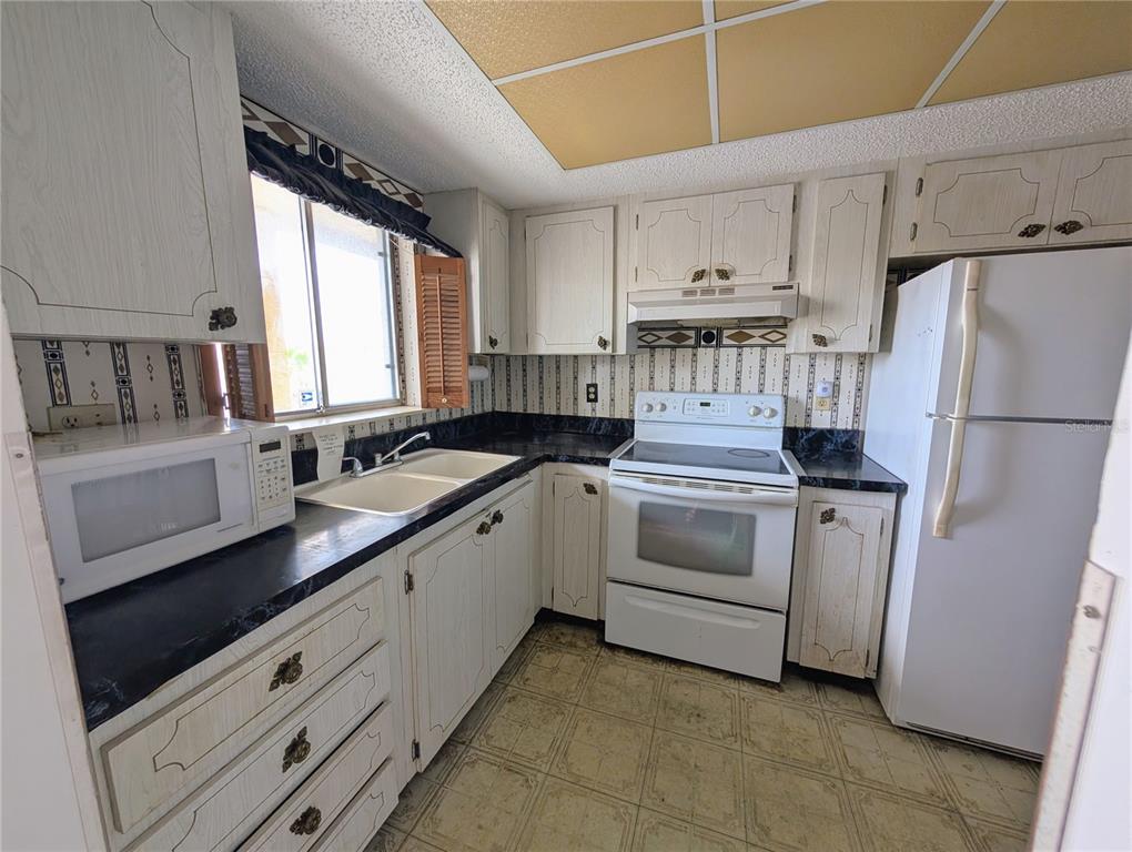 A kitchen features white cabinetry, black countertops, a white stove, and a white refrigerator — 3714 LAKE BAYSHORE DRIVE UNIT K-418, BRADENTON, FL