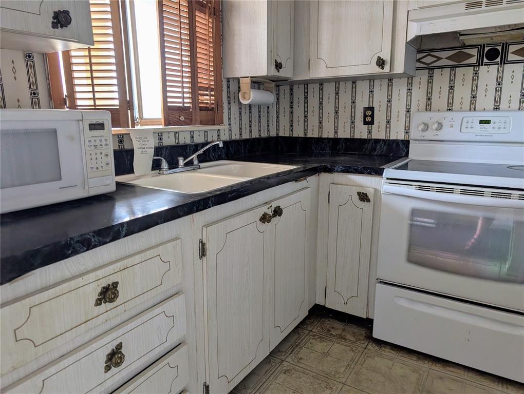 A kitchen features white wood-grain cabinets, black laminate countertops, a white stove, and patterned wallpaper — 3714 LAKE BAYSHORE DRIVE UNIT K-418, BRADENTON, FL