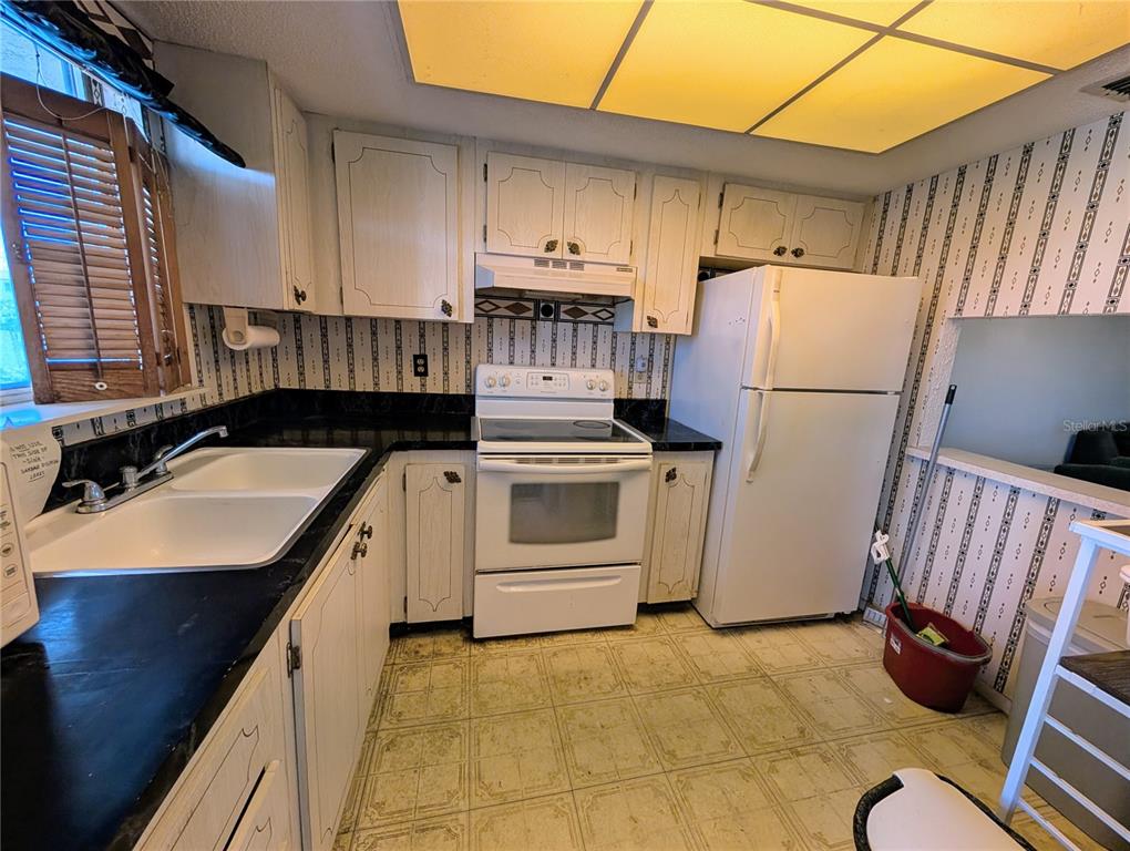A kitchen with white cabinets, black countertops, a white stove, and patterned wallpaper — 3714 LAKE BAYSHORE DRIVE UNIT K-418, BRADENTON, FL