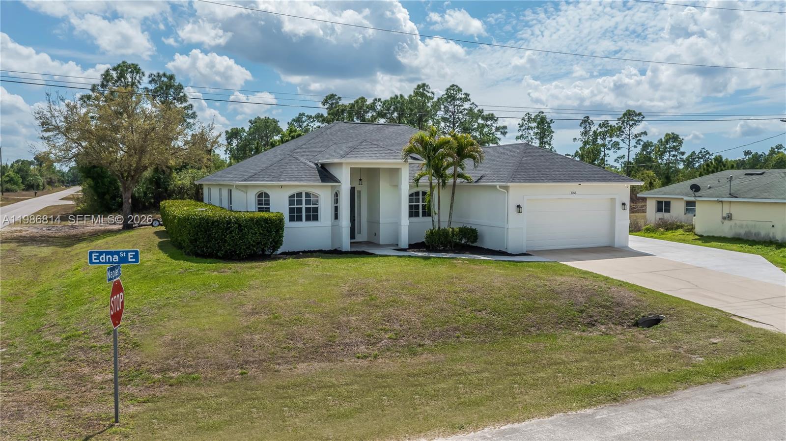 A white single-story house with a dark shingled roof and a two-car garage — 1256 E Edna St., Lehigh Acres FL 33974, LEHIGH ACRES, FL