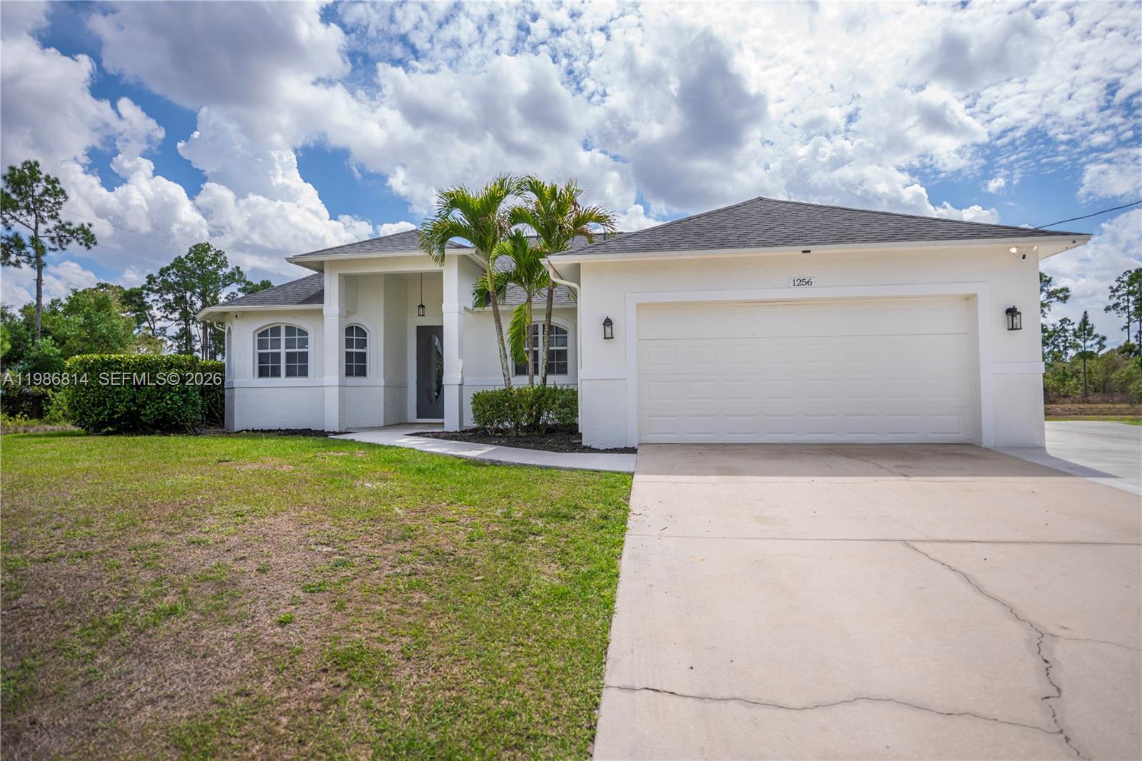 A white single-story house with a two-car garage and a palm tree in front — 1256 E Edna St., Lehigh Acres FL 33974, LEHIGH ACRES, FL